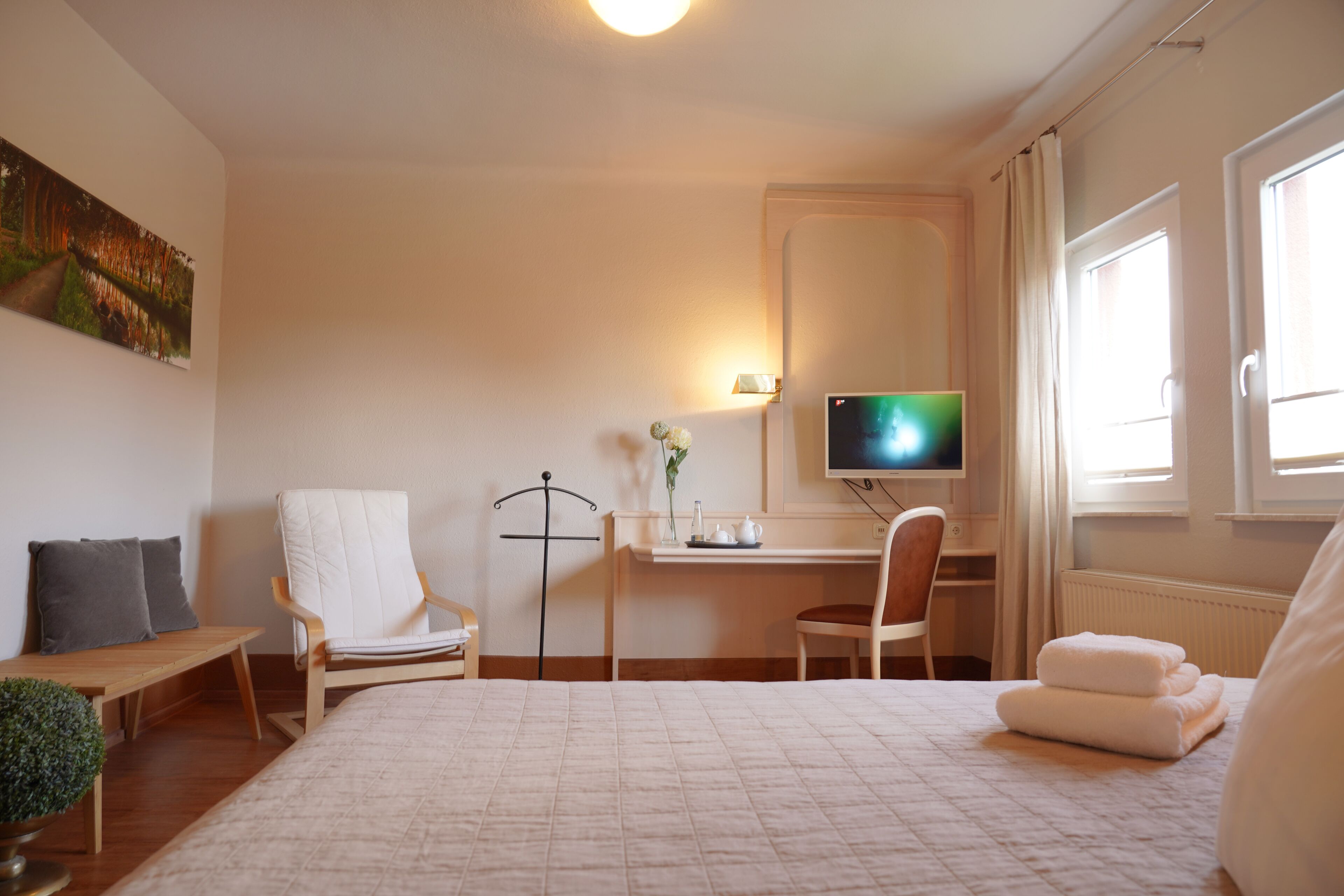 A bedroom with a bed, a desk, a chair, a TV, and a window.