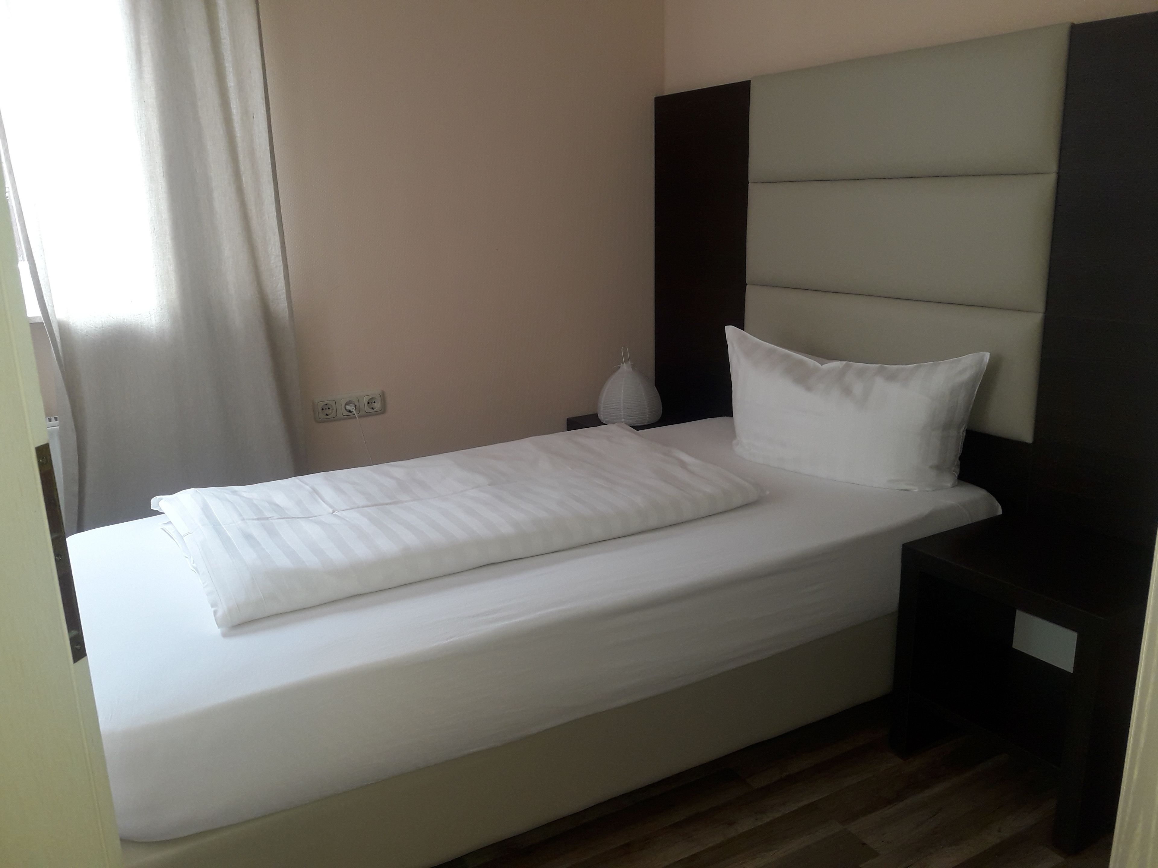 A neatly made bed with white linens in a hotel room.