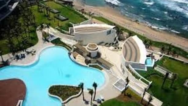 Ein Resort mit großem Pool, direkt am Strand und einem runden Gebäude.
