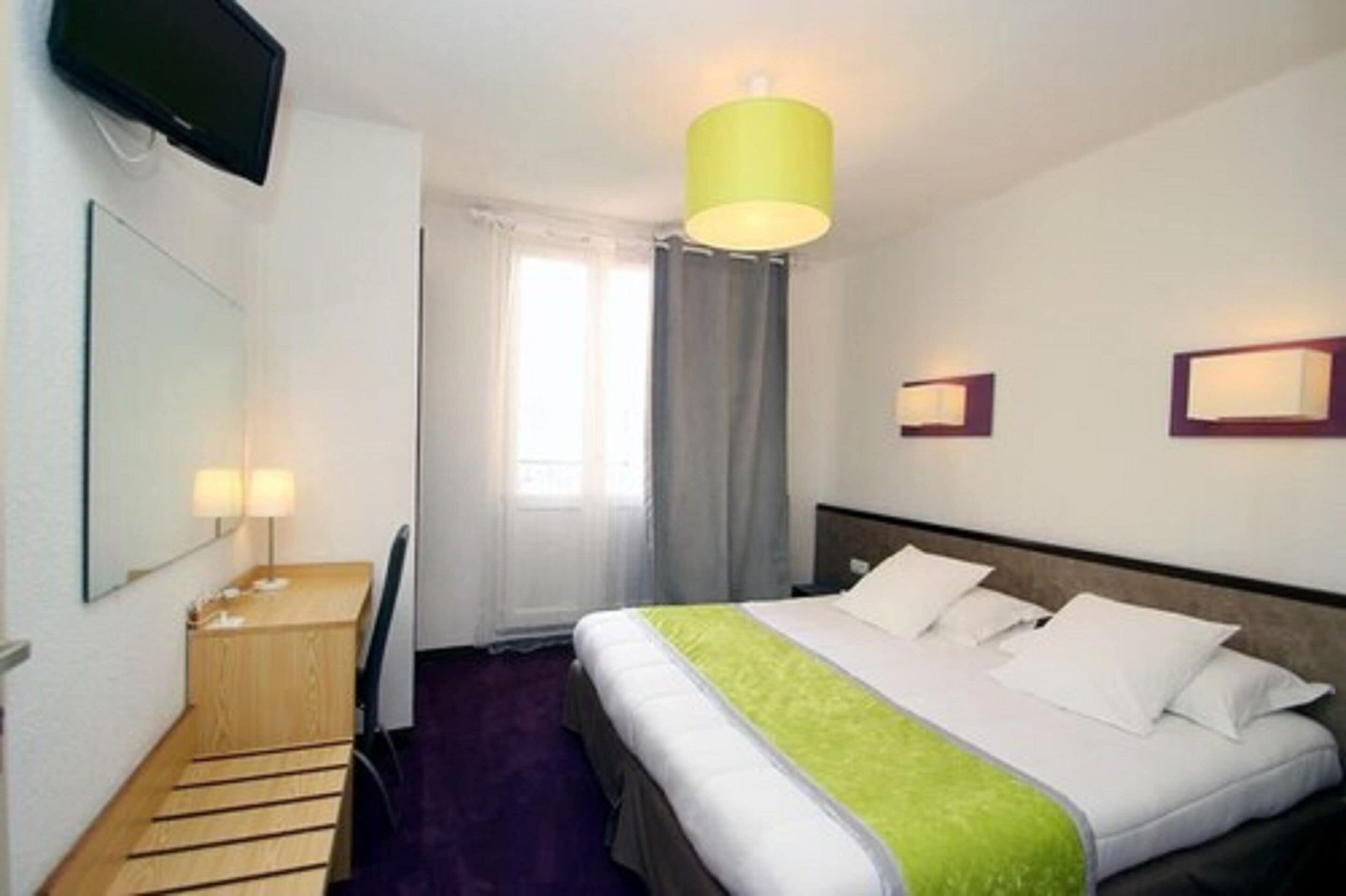 A hotel room with a bed, a desk, a chair, a television, and a window with curtains.