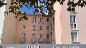 Un hôtel appelé «Peyramale», avec une rangée de chaises blanches à l’extérieur, une entrée bien visible et un balcon doté de rampes en métal.