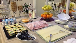 Une table de buffet proposant une variété d’aliments, notamment des fruits, des pâtisseries et des charcuteries.