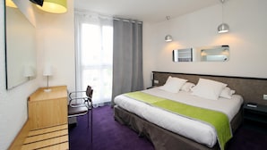 Une chambre d’hôtel avec un lit, un bureau, une chaise, une télévision et une fenêtre avec des rideaux.