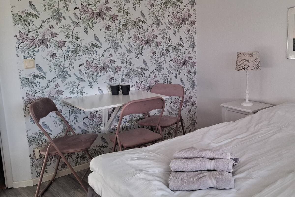 A bedroom with a bed, a desk with two chairs, a lamp, and a framed picture on the wall.