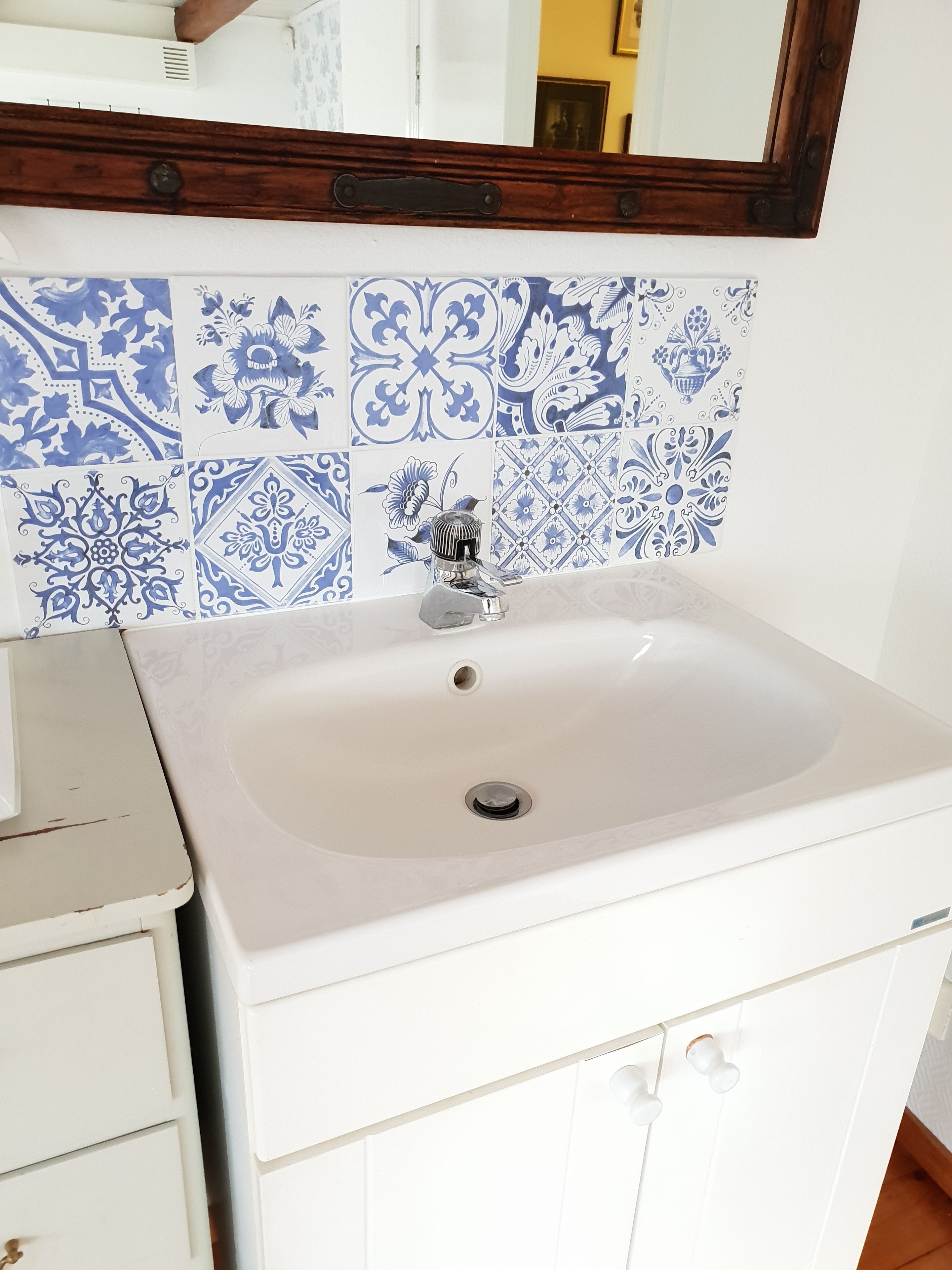 A bathroom with a white sink, blue patterned tiles, and a wooden-framed mirror.