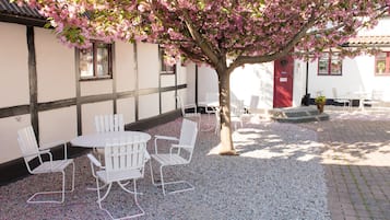 Relax in the serene outdoor seating area with a table and chairs set amidst a picturesque tree with blooming flowers.