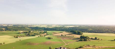 A rural landscape with rolling green fields, a few scattered trees, and a small cluster of buildings in the foreground.