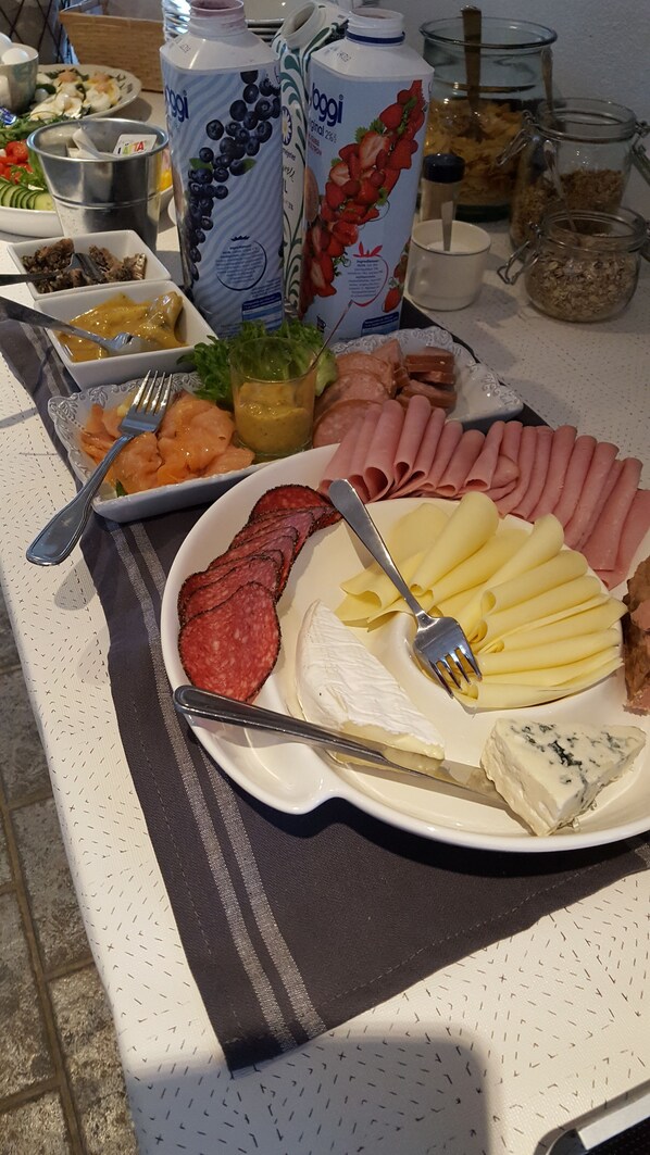 Una mesa de buffet con diversos alimentos, incluyendo carnes cortadas, quesos y una ensalada.