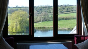 A room with a large window overlooking a river and greenery. There is a table with a white tablecloth and a radiator below it. - Cameley Lodge (Bristol)