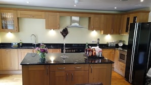 A modern kitchen with wooden cabinets, a central island, and a dining area with a table and chairs. - Cameley Lodge (Bristol)
