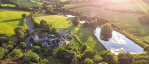 An aerial view of a rural property with a house, a driveway, and a small pond. - Cameley Lodge (Bristol)