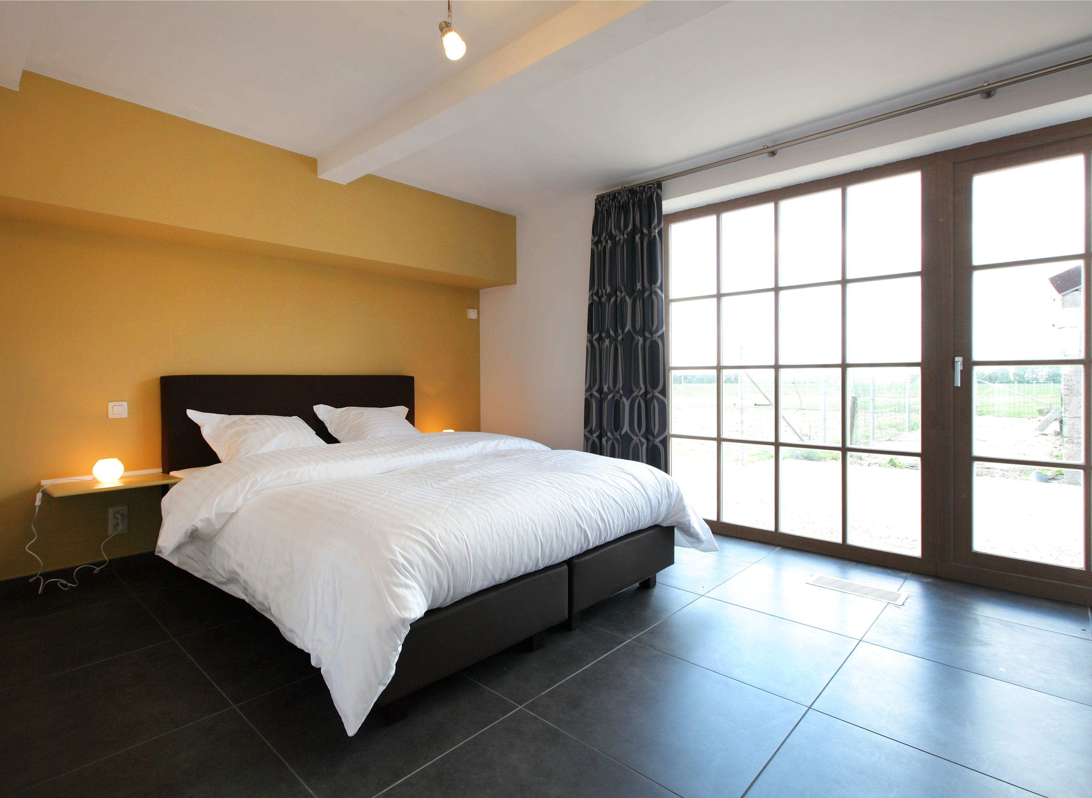 Une chambre à coucher moderne avec un grand lit, une table de chevet et une fenêtre donnant sur l’extérieur.