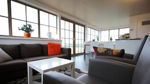 A spacious living area with a sofa, a coffee table, and a chair. There are large windows providing natural light and a view of the outdoors. - B&B Back2Front (Ypres)