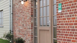 A brick building with a wooden door and two wall-mounted lights. - B&B Back2Front (Ypres)