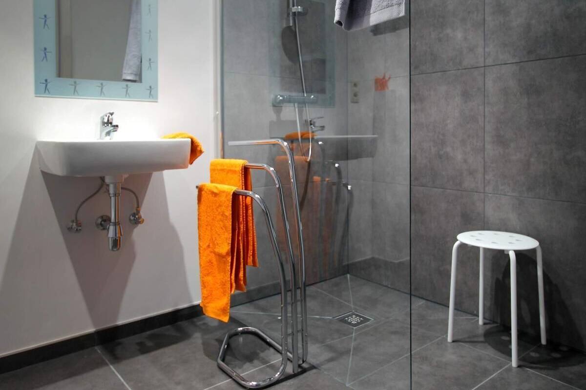 A modern bathroom with a glass shower enclosure, a white sink, and a small white stool.