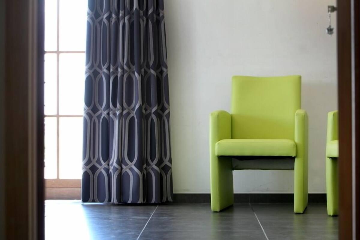 A room with a patterned curtain, a green chair, and a tiled floor.