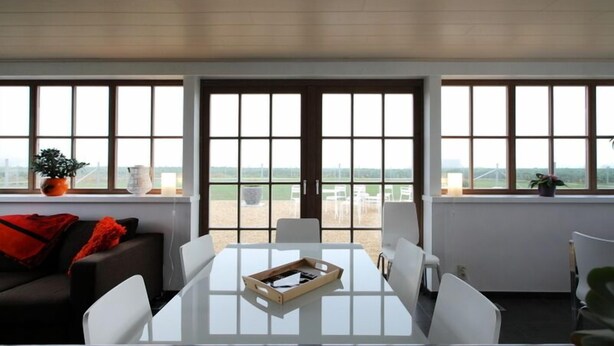 A modern room with a large glass table, white chairs, and a view through large windows. - B&B Back2Front (Ypres)
