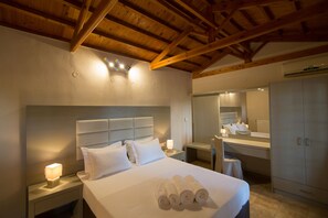 A hotel room with a wooden ceiling, a large bed with white linens, a bedside table with a lamp, a mirror, and a wardrobe. - Vicky Studios (Lesvos)