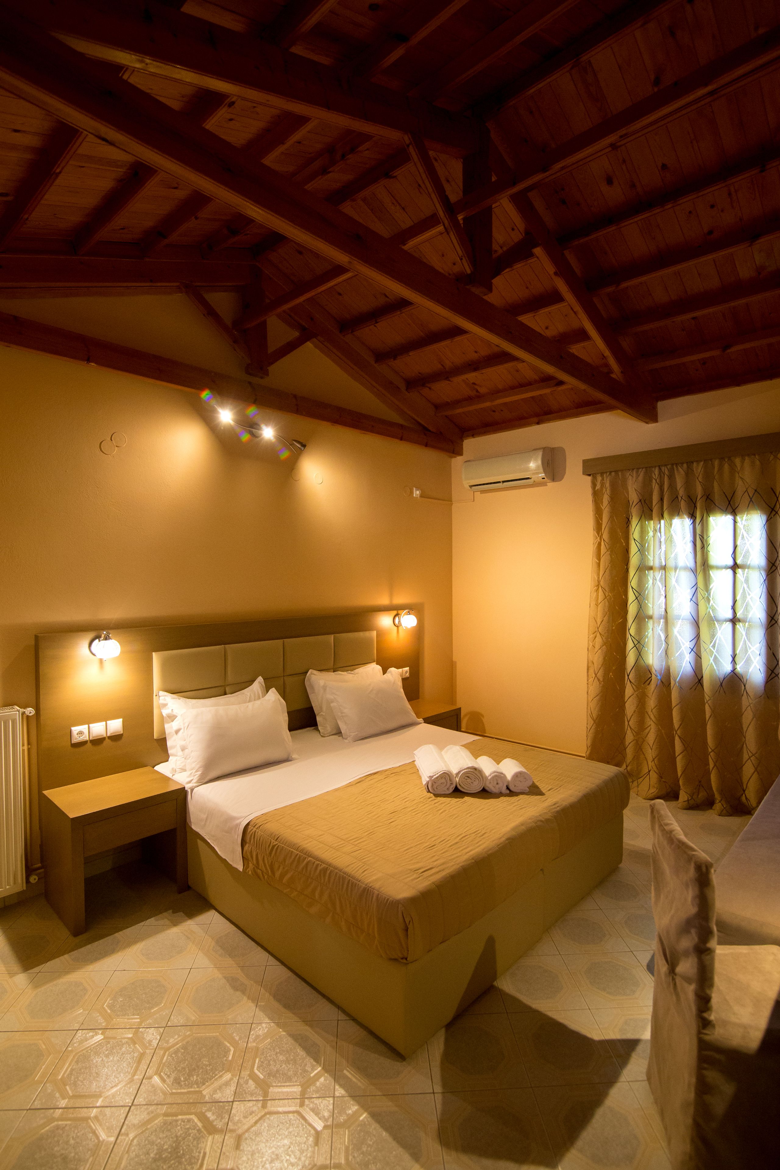 A bedroom with a large bed, a nightstand, a wall-mounted light, and a window with curtains.