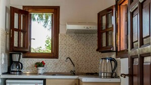 A compact kitchen with wooden cabinets, a built-in dishwasher, and a window with a view of greenery. - Vicky Studios (Lesvos)