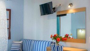 A bedroom with a blue sofa, a wooden bedside table, a mirror, and a television mounted on the wall. - Vicky Studios (Lesvos)