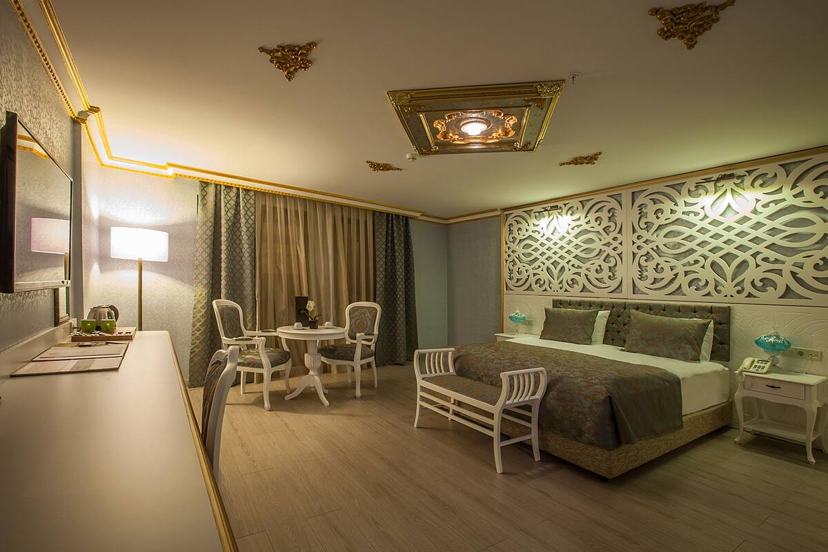A hotel room with a bed, two chairs, a small table, a desk, and a decorative wall panel.