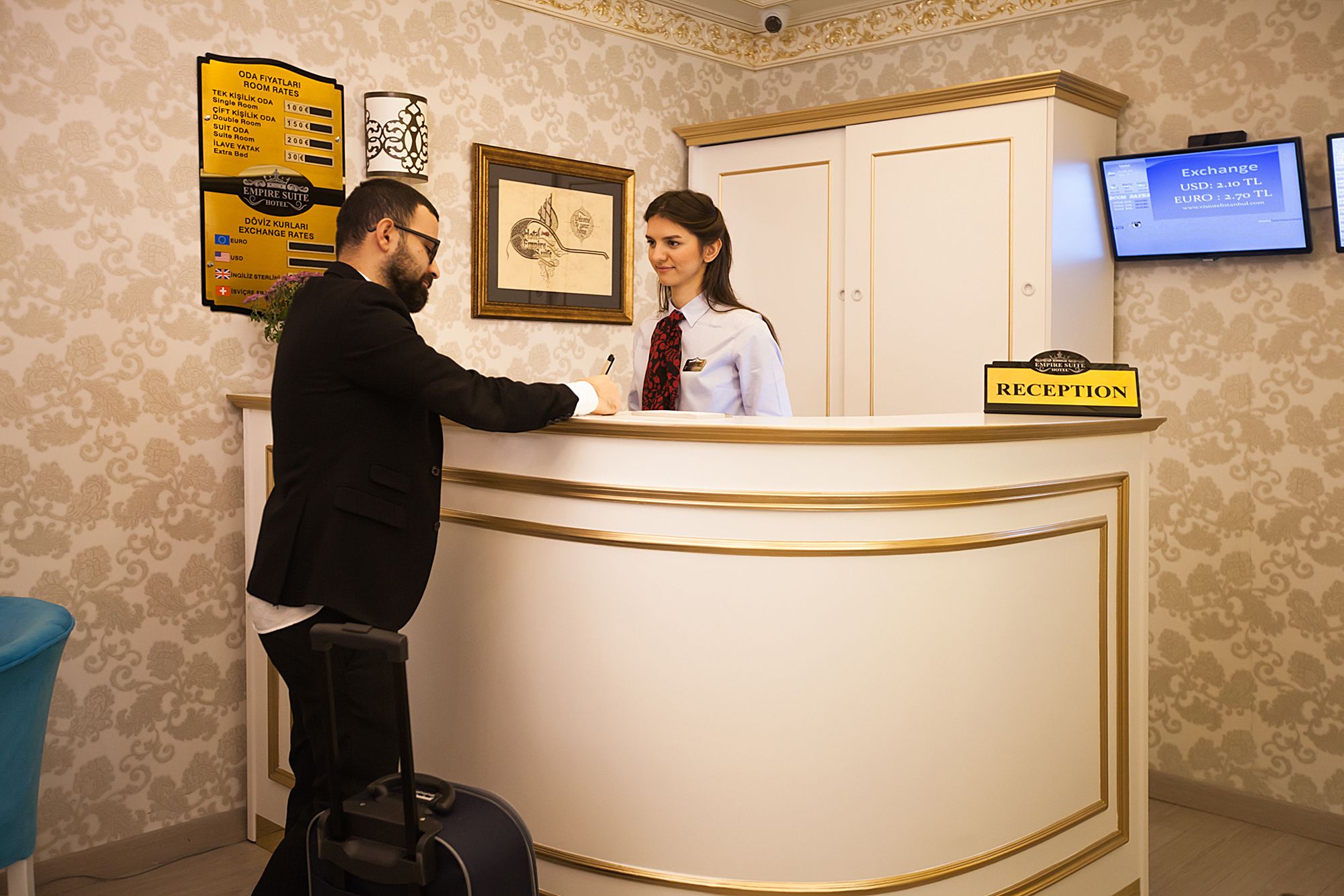 A reception desk with a sign indicating "RECEPTION" and a digital screen displaying exchange rates.