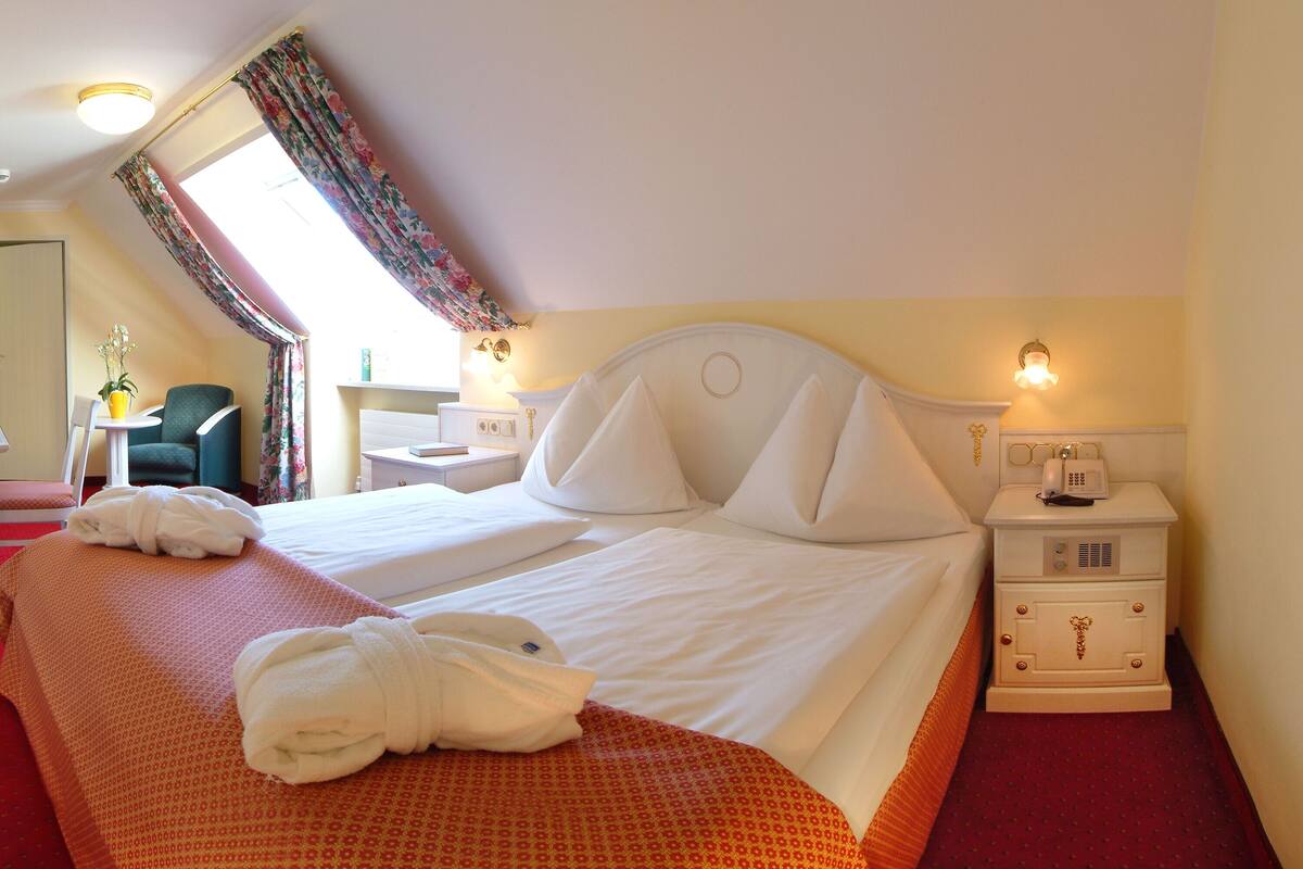 A hotel room with a large bed, a nightstand with a lamp, a chair, and a window with curtains.