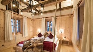 A wooden room with a bed, a chandelier, and a window with curtains.