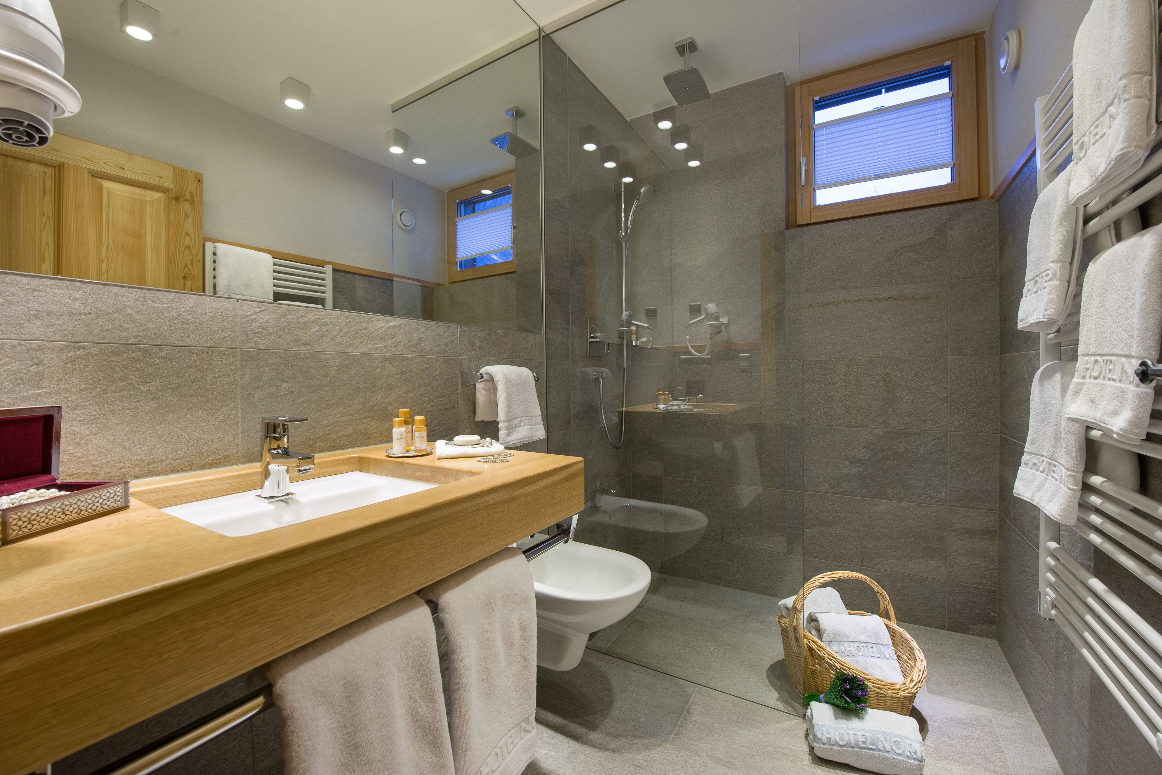 Un baño moderno con tocador de madera, ducha con cerramiento de vidrio y ventana visible.