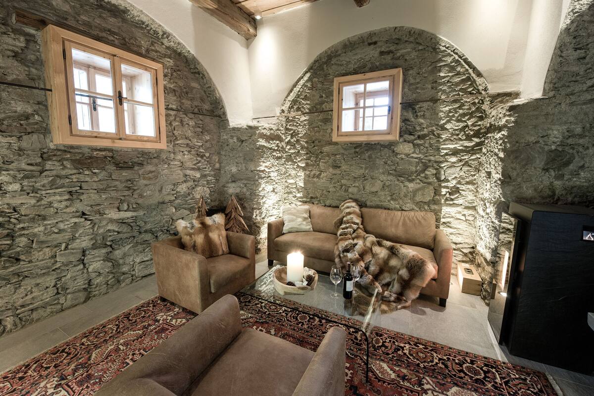 A cozy room with stone walls, two sofas, a glass coffee table with a candle, and a cat.