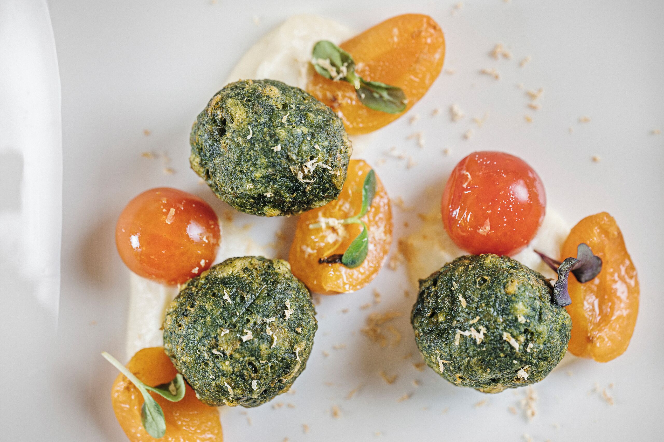 Un plato con comida que incluye hamburguesas verdes, tomates cherry y una salsa cremosa.