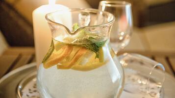 A clear glass pitcher with a beverage and mint leaves on a tray, accompanied by a lit candle and a glass on a wooden table.