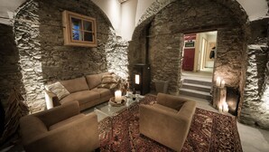A cozy room with stone walls, a wooden window, a sofa, a coffee table, and a patterned rug.