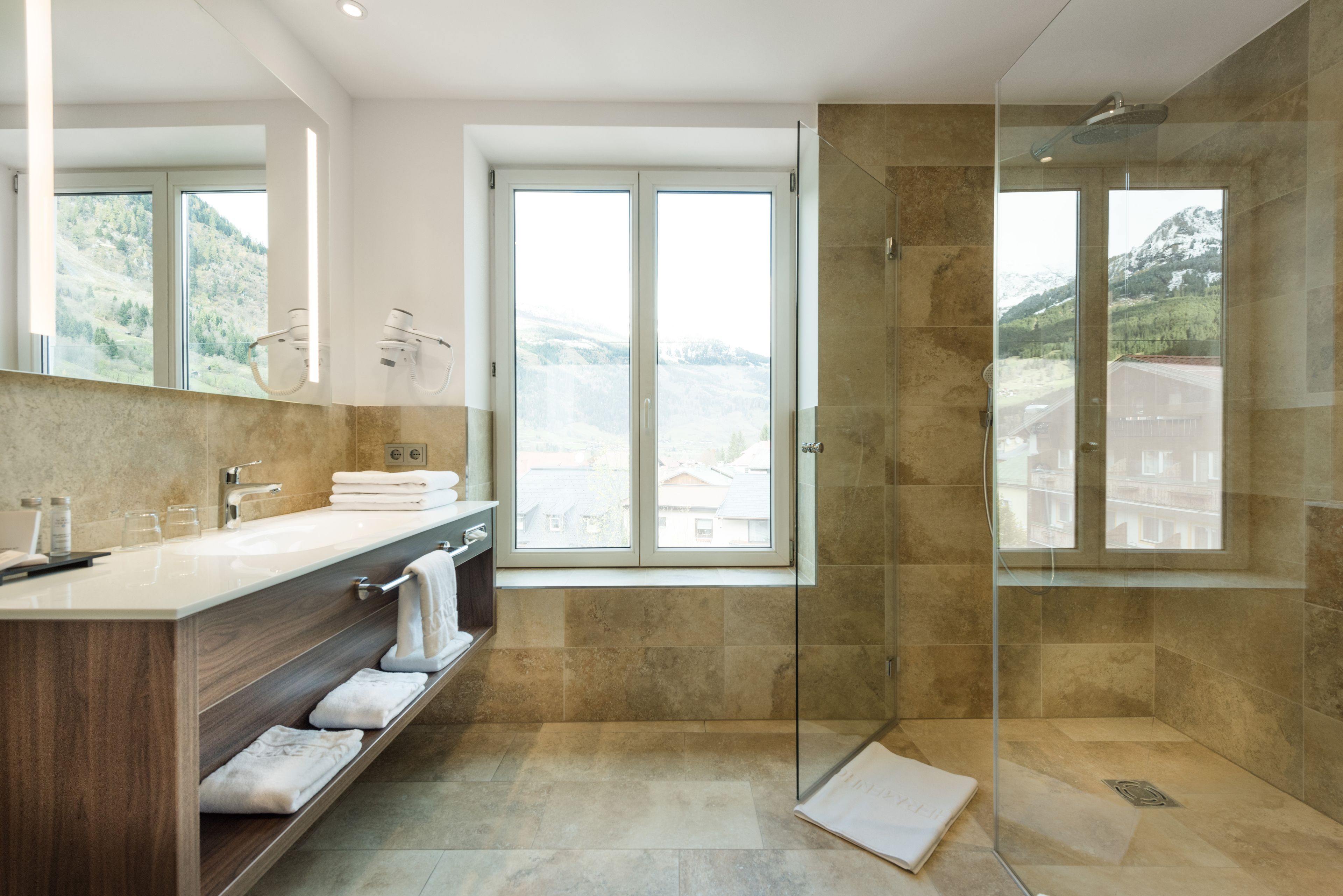 Een moderne badkamer met een douche met glazen wand, een grote spiegel en uitzicht op bergen door de ramen.