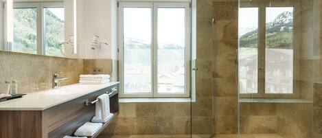 Un baño moderno con ducha envuelta en vidrio, un espejo grande y vistas a montañas a través de las ventanas.
