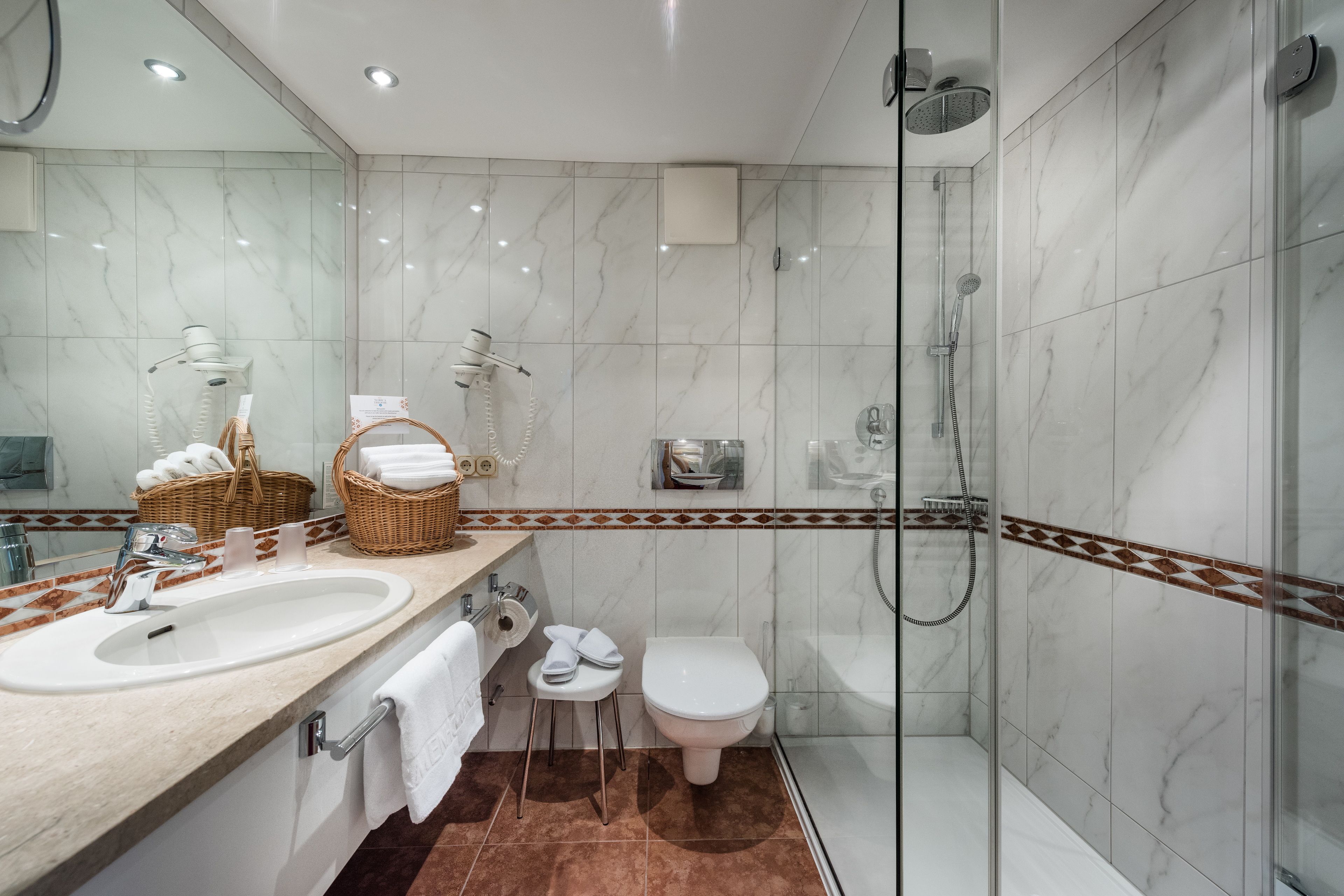 A modern bathroom with a large mirror, two sinks, a toilet, and a glass-enclosed shower area.