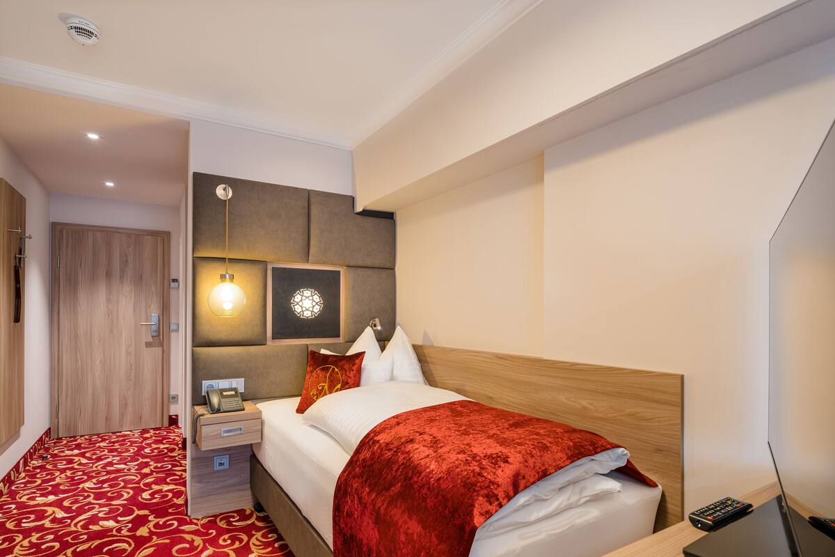 A hotel room with a bed, bedside table, lamp, and a wall-mounted TV.