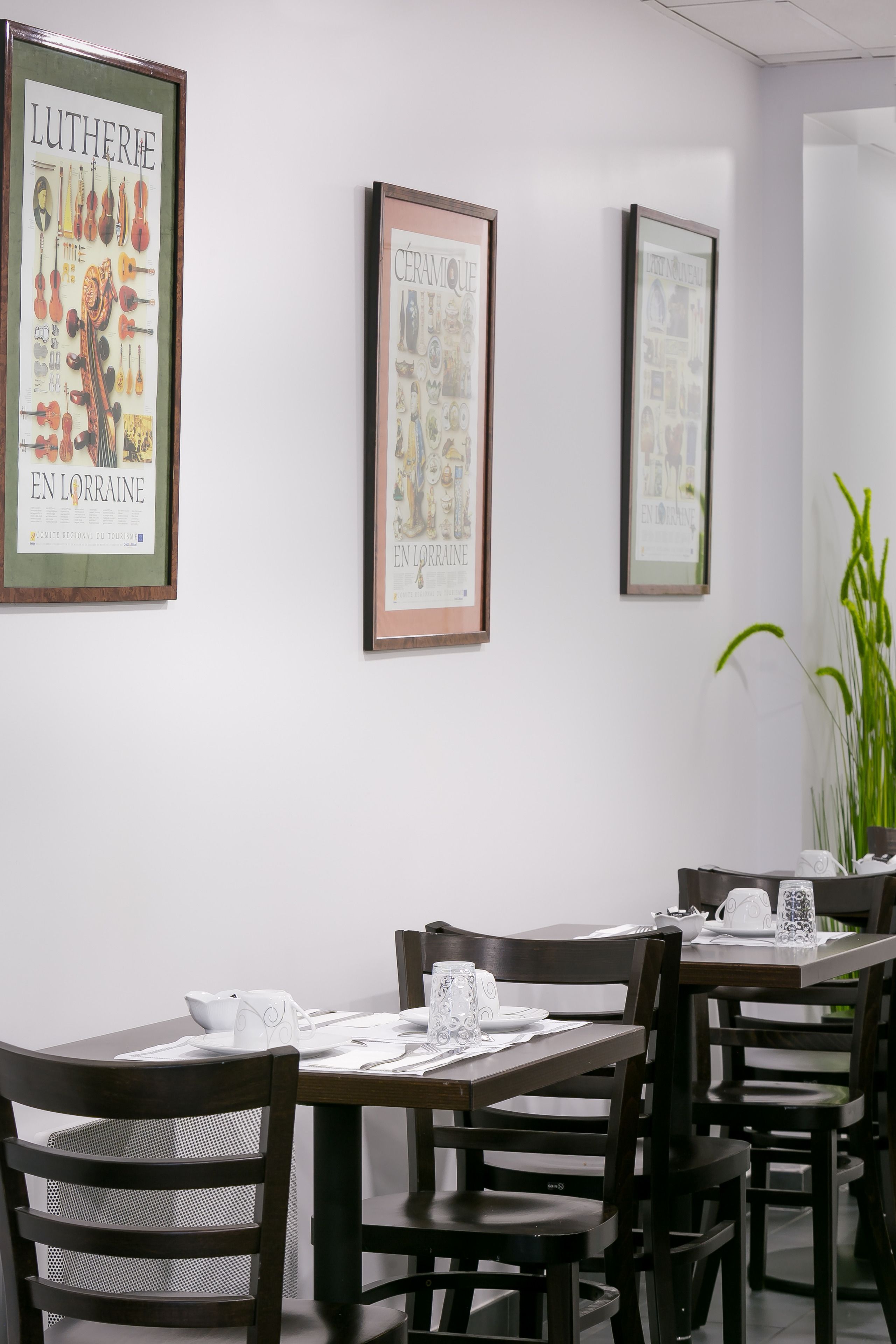 Un comedor con carteles enmarcados en la pared, mesas y sillas de madera, y una planta en maceta.