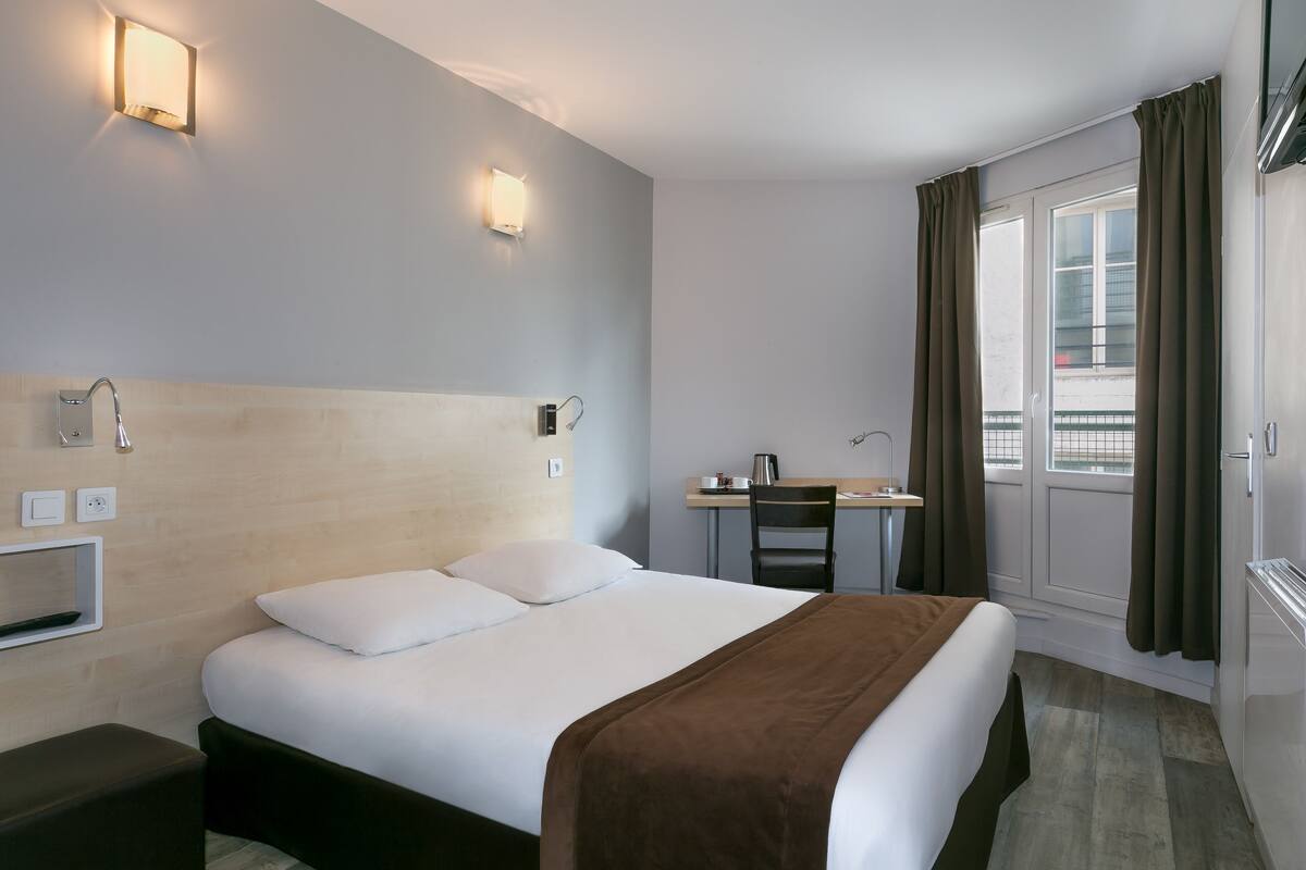 A hotel room with a bed, desk, chair, and a window with curtains.