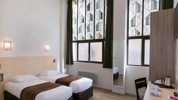 A hotel room with two beds, a desk with a chair, a radiator, and a large window with curtains. - Hotel Foch Nancy Centre Gare (Nancy)