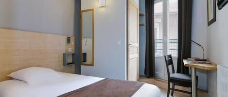 Habitación de hotel con cama, escritorio y silla. Una puerta da acceso a un balcón.