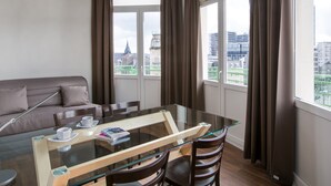 A modern hotel room with a glass dining table, brown leather sofa, and large windows offering city views. - Hotel Foch Nancy Centre Gare (Nancy)