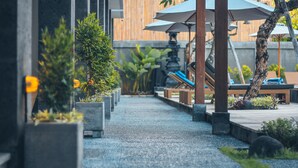 A pathway lined with potted plants and outdoor seating under umbrellas, leading to a wooden deck area. - Kubu Cempaka Seminyak Hotel (Seminyak)