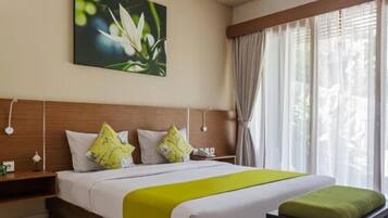 Una camera d'albergo con un letto grande, due cuscini, una coperta verde, un comodino con una lampada e un quadro con fiori sulla parete.