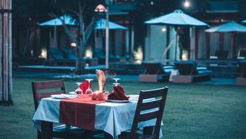 Un área de comedor al aire libre con mesas dispuestas para dos, cada una con mantel blanco y servilletas rojas.