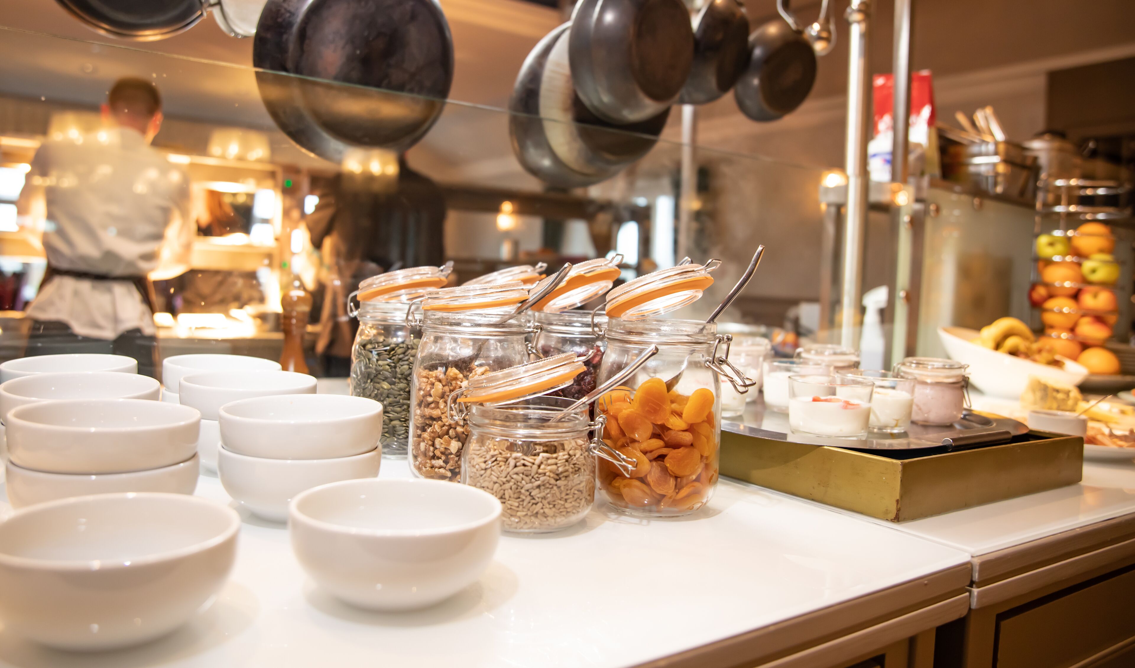 A buffet setup with various food items in jars and bowls, a fruit display, and kitchen utensils in the background.