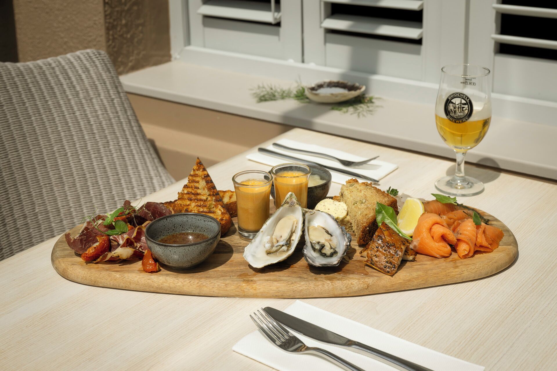 A meal with grilled bread, oysters, smoked salmon, and a glass of wine on a wooden table.