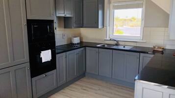 A kitchen with grey cabinets, a black oven, a toaster, and a window with a view of the outdoors.