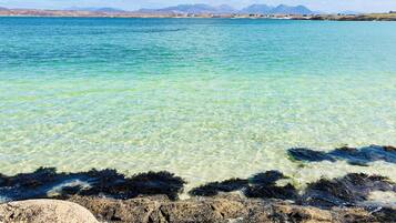 Experience the serene beauty of the coastline with clear waters and a stunning mountain range in the distance.